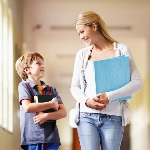 Eine lächelnde Sozialarbeiterin spricht mit einem Jungen auf dem Schulflur